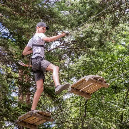 Teenager having fun on high ropes course, adventure, park, climbing trees in a forest in summer